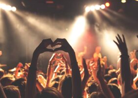 Concert goers raise hands in heart gesture.