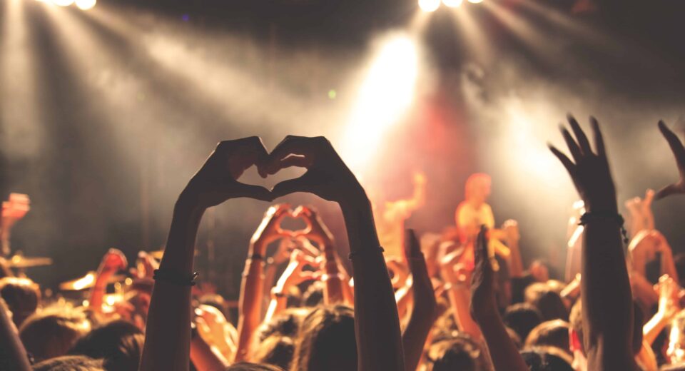 Concert goers raise hands in heart gesture.